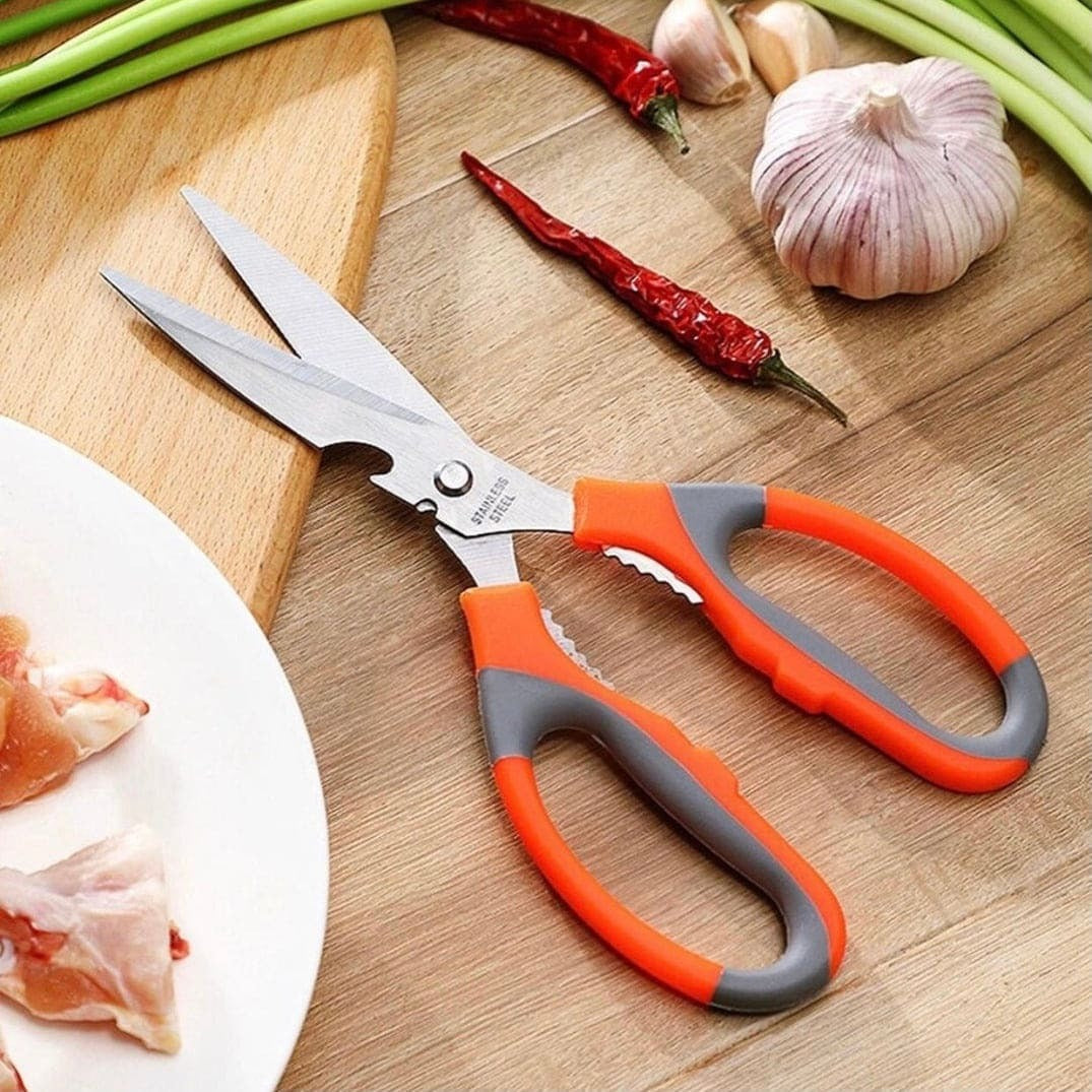 Kitchen shears with orange and gray handles on a wooden cutting board with vegetables.