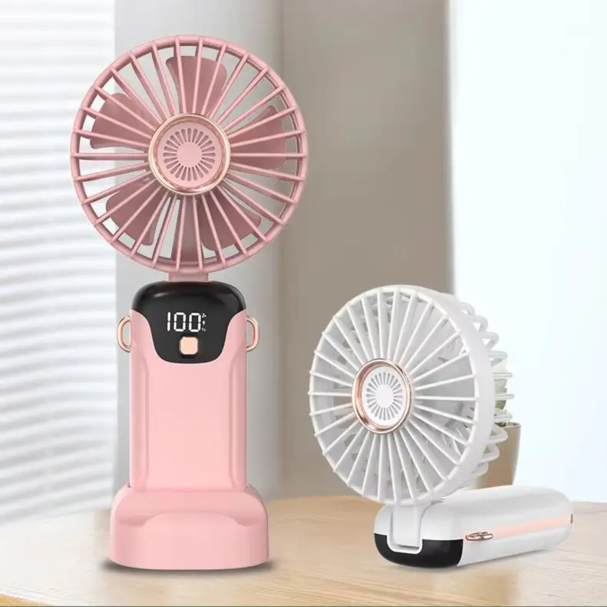 Pink handheld fan with digital display on a wooden surface.
