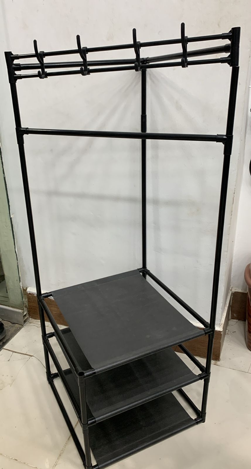 Black metal clothing rack with shelves against a white wall.