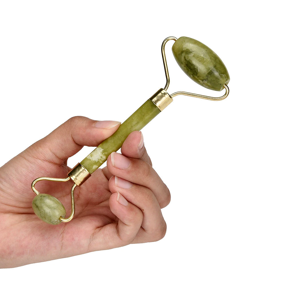 Hand holding a green jade roller with gold accents on a white background