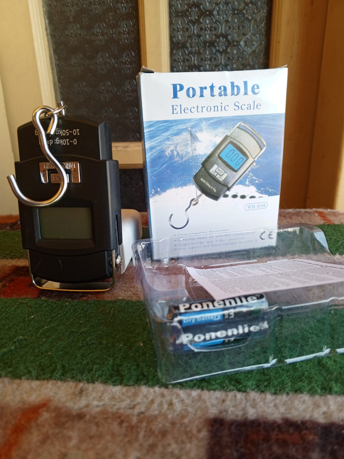 Portable electronic scale with packaging and batteries on a carpeted floor