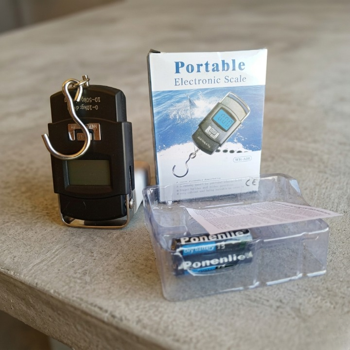 Portable electronic scale with packaging and batteries on a beige surface