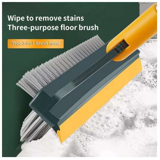 A three-in-one floor cleaning brush with a yellow handle, dark gray plastic frame, and dual bristle heads, shown cleaning a green wall with white cleaning foam. Text on the image reads 'Wipe to remove stains' and 'Three-purpose floor brush'.