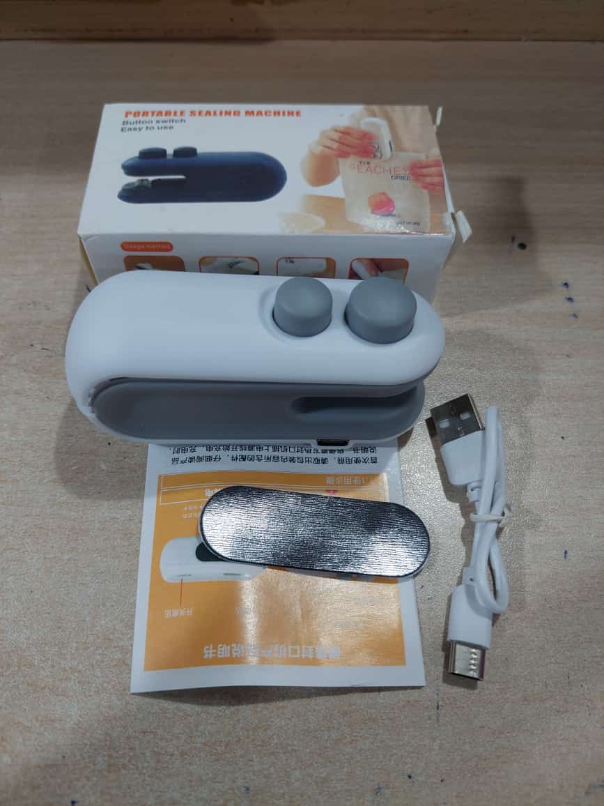 Portable sealing machine with packaging, USB cable, and manual on a wooden surface