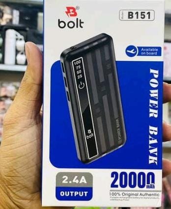 A hand holding a Bolt B151 20000mAh power bank box in a retail store setting. The packaging is white and blue with a graphic of the black power bank.