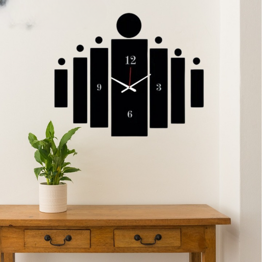 Black wall clock with unique design on a white wall above a wooden table with a plant.