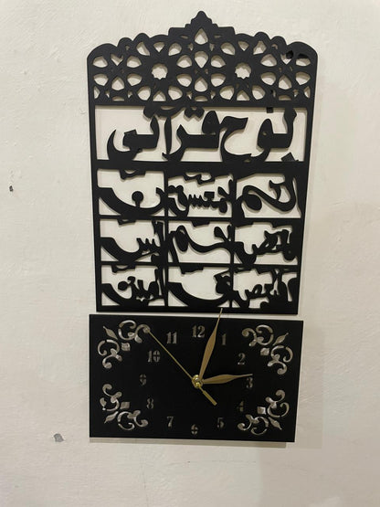 Black metal Islamic wall clock featuring Arabic calligraphy of Ayat al-Kursi and a square clock face with gold hands, mounted on a white wall.