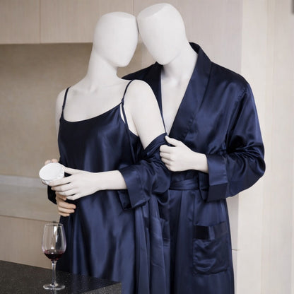 Two mannequins wearing navy satin robes with a glass of red wine on a table.