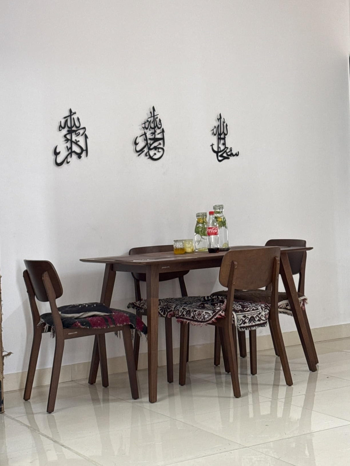 Dining table set with chairs against a white wall with Arabic calligraphy.