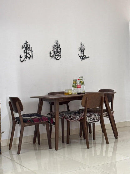 Dining table set with chairs against a white wall with Arabic calligraphy.