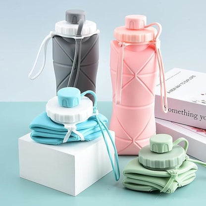 Set of three collapsible water bottles in gray, pink, and green on a light blue background.